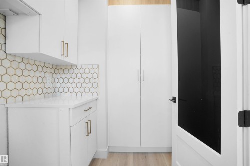 White cabinetry featuring gold-toned hardware, hexagon tile backsplash, light-toned wood-finish flooring, and a full-height storage cabinet - 22139 81 Avenue, Edmonton, AB - Indoor Photo Showing Other Room