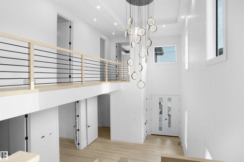 Two-story foyer featuring a contemporary chandelier, light wood-finish flooring, multiple windows, and a second-story landing with a cable railing system - 22139 81 Avenue, Edmonton, AB - Indoor Photo Showing Other Room