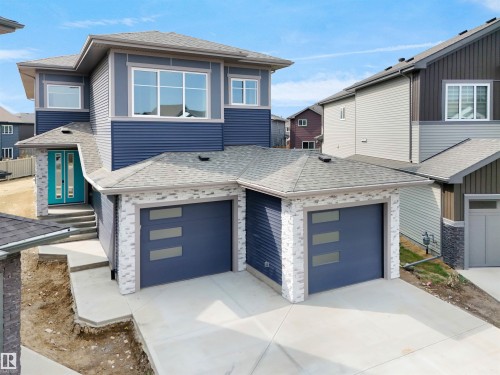Contemporary exterior featuring blue horizontal siding, a light teal double entry door, and a two-car garage with frosted panel inserts - 22139 81 Avenue, Edmonton, AB - Outdoor