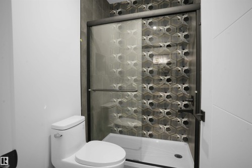Full bathroom featuring a walk-in shower with a black-framed glass enclosure, unique hexagonal patterned shower tile, and a built-in shower niche - 22139 81 Avenue, Edmonton, AB - Indoor Photo Showing Bathroom