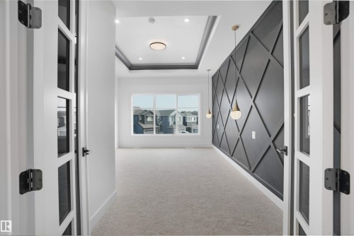 Room featuring a decorative accent wall with geometric paneling, pendant lighting, large window, tray ceiling, and recessed lighting - 22139 81 Avenue, Edmonton, AB - Indoor Photo Showing Other Room