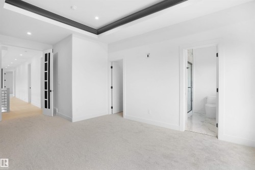 Spacious room featuring light-colored carpeting, a tray ceiling with dark trim, recessed lighting, and a doorway revealing a bathroom with marble-finish flooring and a shower enclosure - 22139 81 Avenue, Edmonton, AB - Indoor Photo Showing Other Room