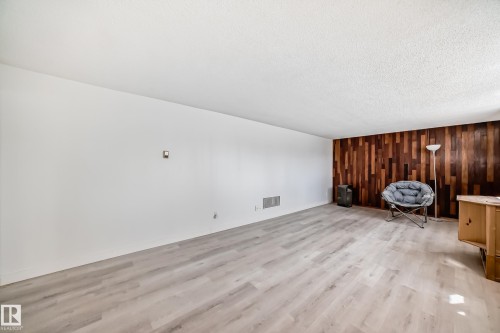 Spacious interior room featuring light wood-finish flooring, a textured white ceiling, and a wall accented with varied wood paneling - 12825 102 Street, Edmonton, AB - Indoor Photo Showing Other Room