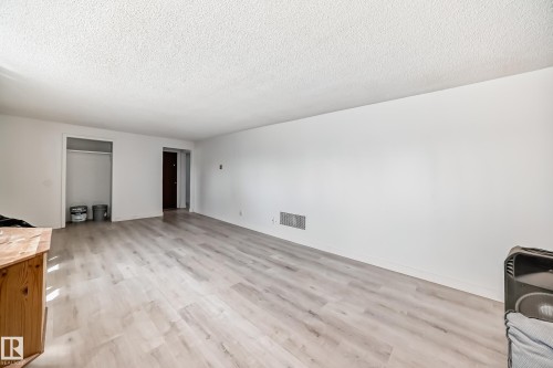 Spacious room featuring light wood-finish flooring, white painted walls, and a textured white ceiling - 12825 102 Street, Edmonton, AB - Indoor Photo Showing Other Room