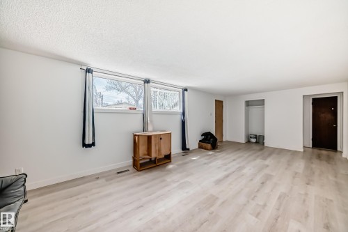 Expansive room featuring light wood-finish flooring, white walls, and multiple windows with curtain rods - 12825 102 Street, Edmonton, AB - Indoor