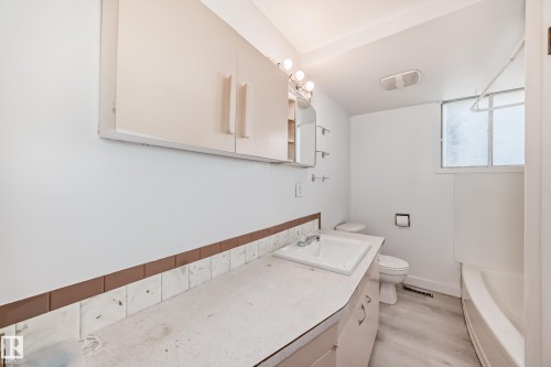 Bathroom featuring a single vanity with an integrated sink, overhead wall cabinets, and a bathtub with shower - 12825 102 Street, Edmonton, AB - Indoor Photo Showing Laundry Room