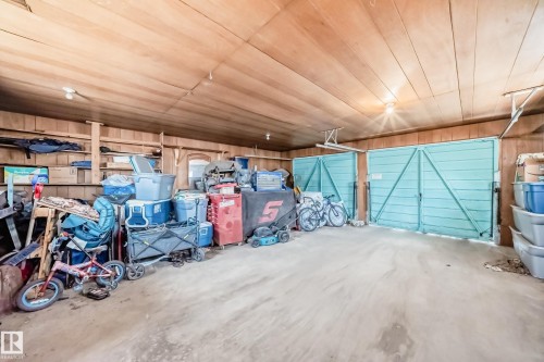 Garage space featuring two light blue double doors, wood paneling on walls and ceiling, and exposed ceiling light fixtures - 12825 102 Street, Edmonton, AB - Indoor Photo Showing Garage