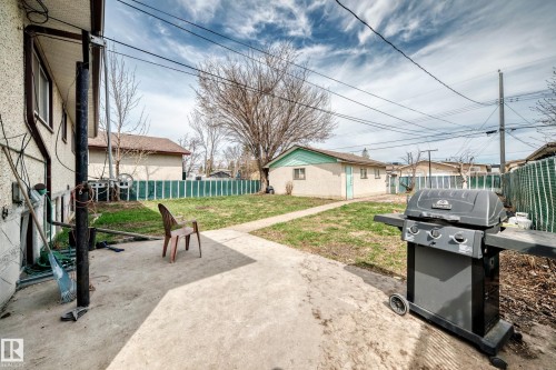Expansive backyard featuring a concrete patio, a detached storage building with light green trim, and a partially fenced perimeter - 12825 102 Street, Edmonton, AB - Outdoor