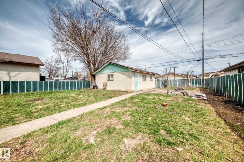 Spacious backyard featuring a concrete pathway, a detached structure with light stucco finish and green trim, and established perimeter fencing - 12825 102 Street, Edmonton, AB - Outdoor