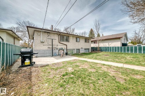 Spacious backyard featuring a chain-link fence, concrete patio, and mature trees - 12825 102 Street, Edmonton, AB - Outdoor With Exterior
