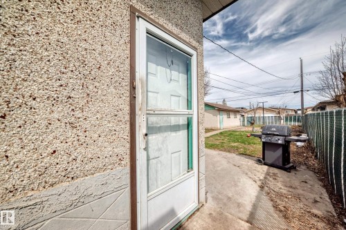 Textured stucco exterior with a storm door entry, concrete walkway, and fenced yard - 12825 102 Street, Edmonton, AB - Outdoor