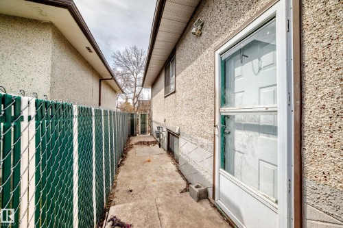 Side exterior featuring a concrete pathway, privacy fencing with green slats, and an exterior door with a storm door - 12825 102 Street, Edmonton, AB - Outdoor With Exterior
