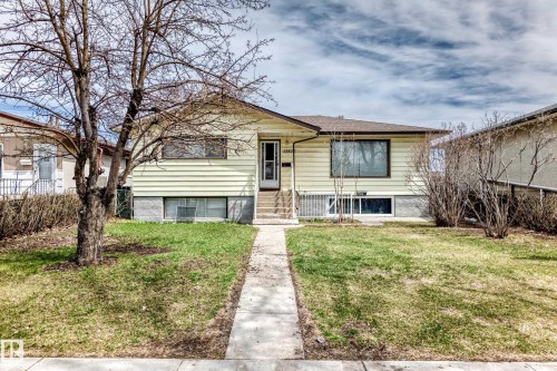 Bungalow residence featuring light yellow siding, a prominent front entrance with a white door, and a concrete pathway leading to the street - 12825 102 Street, Edmonton, AB - Outdoor