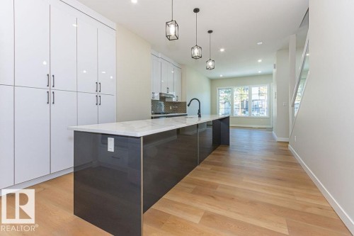 Kitchen featuring an extended center island with a light-toned countertop, a matte black faucet, and three pendant light fixtures - 9814 155 Street, Edmonton, AB - Indoor
