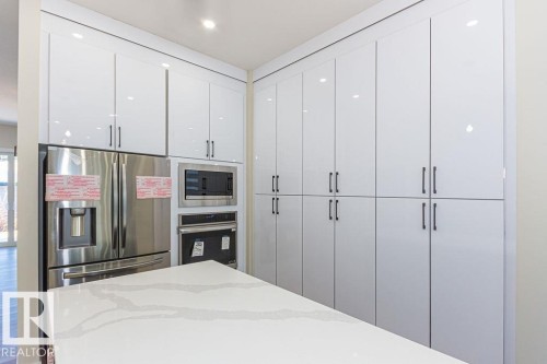 Contemporary kitchen featuring extensive white high-gloss cabinetry with black hardware, a stainless steel French door refrigerator, built-in microwave, and an integrated oven - 9814 155 Street, Edmonton, AB - Indoor Photo Showing Other Room