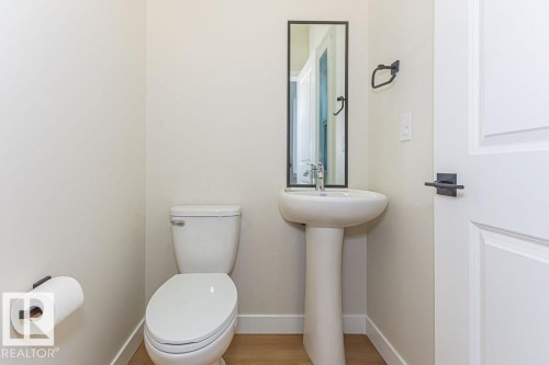 Pedestal sink with a black-framed mirror, complemented by a white toilet and wood-finish flooring - 9814 155 Street, Edmonton, AB - Indoor Photo Showing Bathroom