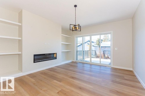 Spacious room featuring wood-finish flooring, a built-in electric fireplace, integrated shelving on both sides, a contemporary chandelier, and sliding glass doors leading to an exterior area - 9814 155 Street, Edmonton, AB - Indoor With Fireplace