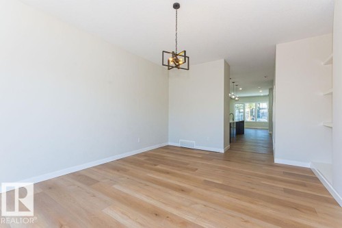 Spacious room featuring wood-finish flooring, a contemporary geometric light fixture, white baseboards, and built-in shelving - 9814 155 Street, Edmonton, AB - Indoor Photo Showing Other Room