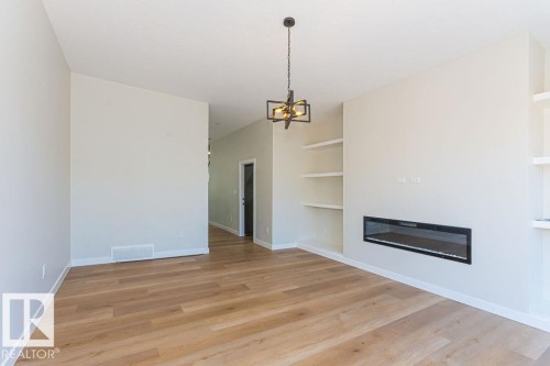 Spacious room featuring wood-finish flooring, a built-in linear fireplace, integrated shelving, and a contemporary ceiling fixture - 9814 155 Street, Edmonton, AB - Indoor With Fireplace