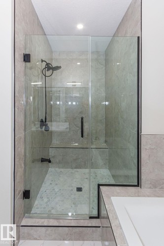 Glass-enclosed shower featuring a built-in bench, pebbled flooring, matte black fixtures, and full-height wall tiling - 9814 155 Street, Edmonton, AB - Indoor Photo Showing Bathroom