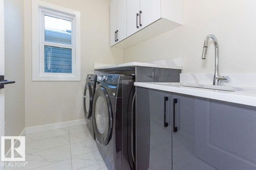 Dedicated laundry area featuring a built-in sink, white stone-finish countertops, and under-cabinet storage - 9814 155 Street, Edmonton, AB - Indoor Photo Showing Laundry Room