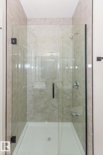 Frameless glass shower enclosure with matte black hardware, textured tile surround, built-in shelving, and a white shower base - 9814 155 Street, Edmonton, AB - Indoor Photo Showing Bathroom