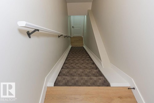 Stairwell featuring light wood-finish flooring, a textured carpet runner, white baseboards, and a white handrail with dark brackets - 9814 155 Street, Edmonton, AB - Indoor Photo Showing Other Room