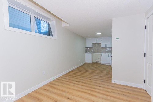 Open concept living space featuring wood-finish flooring, a contemporary kitchenette with white cabinetry and tiled backsplash, a white trim window, and recessed lighting - 9814 155 Street, Edmonton, AB - Indoor Photo Showing Other Room