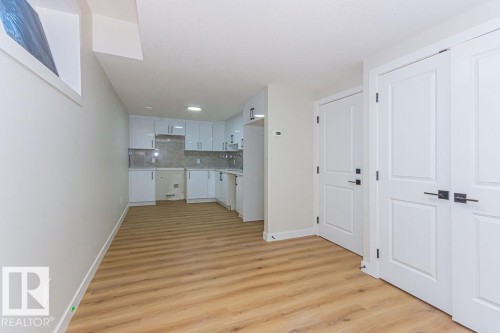 Contemporary kitchen area featuring white cabinetry, light-toned wood-finish flooring, and a window - 9814 155 Street, Edmonton, AB - Indoor