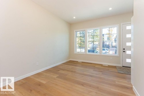 Expansive room featuring wood-finish flooring, recessed lighting, and a modern entry door with frosted glass panels - 9814 155 Street, Edmonton, AB - Indoor Photo Showing Other Room