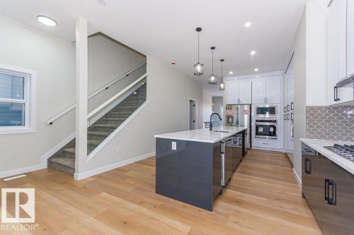 Modern kitchen featuring a central island with a waterfall countertop, integrated sink, and pendant lighting - 9814 155 Street, Edmonton, AB - Indoor Photo Showing Kitchen With Upgraded Kitchen