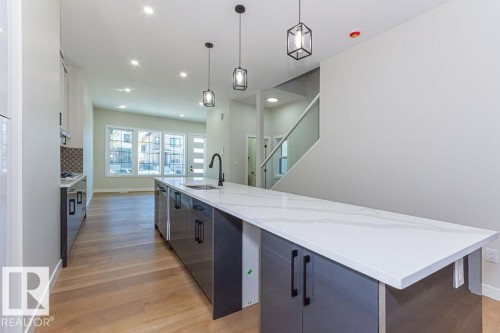 Expansive kitchen island featuring a waterfall-edge countertop and integrated sink with matte black faucet - 9814 155 Street, Edmonton, AB - Indoor Photo Showing Kitchen With Upgraded Kitchen