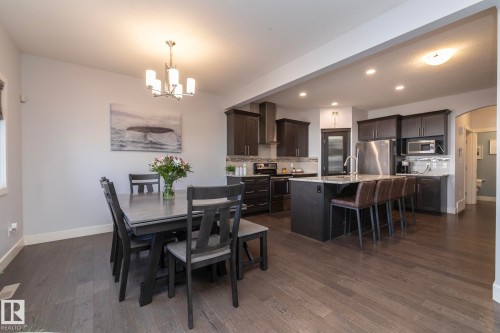 Open-concept kitchen and dining area featuring wood-finish flooring, dark wood cabinetry, a large kitchen island with seating, stainless steel appliances, and recessed lighting - 2016 Redtail Common, Edmonton, AB - Indoor Photo Showing Dining Room