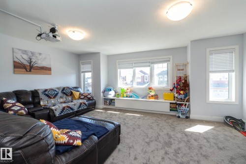 Spacious room featuring light gray wall paint, an integrated ceiling-mounted projector, multiple windows with blinds, a built-in window bench, and light gray carpeted flooring - 2016 Redtail Common, Edmonton, AB - Indoor Photo Showing Living Room
