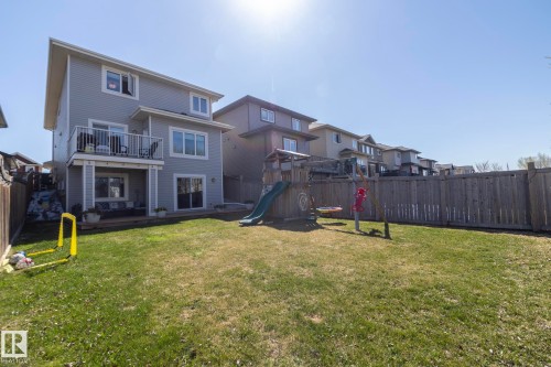 Spacious fenced backyard featuring a manicured lawn, an elevated deck with black metal railings, and a ground-level patio - 2016 Redtail Common, Edmonton, AB - Outdoor