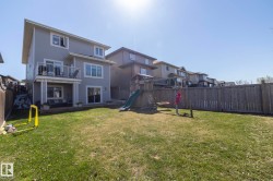 Spacious fenced backyard featuring a manicured lawn, an elevated deck with black metal railings, and a ground-level patio - 