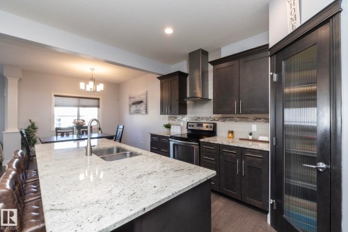 Kitchen featuring a large island with a double basin sink, stainless steel appliances, dark wood-finish cabinetry, and light-toned countertops - 2016 Redtail Common, Edmonton, AB - Indoor Photo Showing Kitchen With Double Sink With Upgraded Kitchen