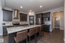 Spacious kitchen featuring an expansive center island with stone-finish countertop, dark wood-finish cabinetry, stainless steel appliances, and wood-finish flooring - 