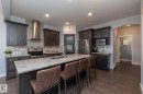 Spacious kitchen featuring an expansive center island with stone-finish countertop, dark wood-finish cabinetry, stainless steel appliances, and wood-finish flooring - 2016 Redtail Common, Edmonton, AB  - Indoor Photo Showing Kitchen With Upgraded Kitchen 