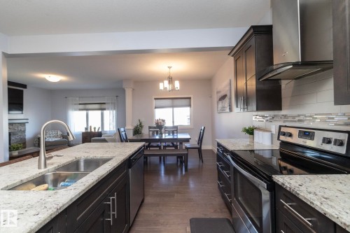 Gourmet kitchen featuring a granite island with undermount sink, stainless steel appliances, dark wood-finish cabinetry, and a tile backsplash - 2016 Redtail Common, Edmonton, AB - Indoor Photo Showing Kitchen With Double Sink With Upgraded Kitchen