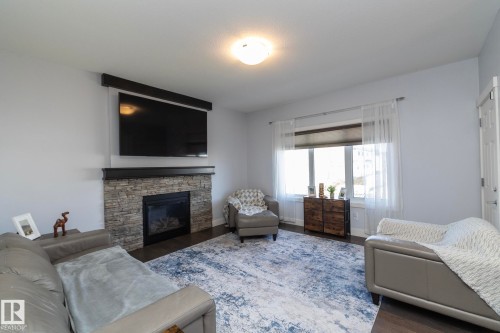Living area featuring a stone-faced fireplace with a dark wood mantel, recessed gas insert, and dark wood-finish flooring - 2016 Redtail Common, Edmonton, AB - Indoor Photo Showing Living Room With Fireplace