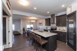 Kitchen featuring an island with granite-style countertop, dark wood-finish cabinetry, stainless steel appliances, and a tiled backsplash - 