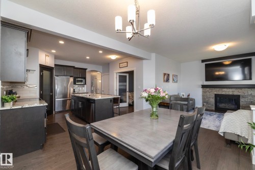 Open-concept living area featuring a kitchen with dark cabinetry, stainless steel appliances, a center island with sink, and light-toned countertops - 2016 Redtail Common, Edmonton, AB - Indoor Photo Showing Dining Room