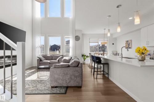 Open-concept living area featuring wood-finish flooring, a kitchen island with pendant lighting, and a living room with high ceilings and tall windows - 1471 Plum Circle Circle, Edmonton, AB - Indoor Photo Showing Other Room