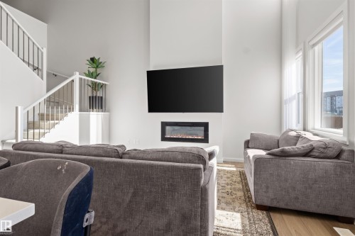 Living space featuring a wall-mounted electric fireplace, light wood-finish flooring, and a multi-level staircase with white railing and dark balusters - 1471 Plum Circle Circle, Edmonton, AB - Indoor Photo Showing Living Room With Fireplace