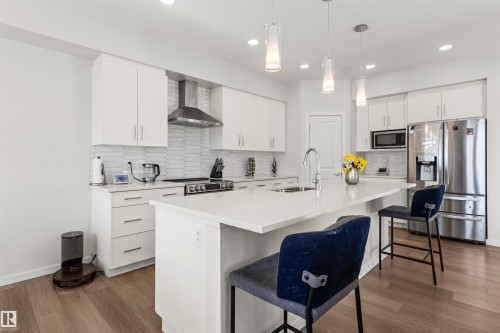 Modern kitchen featuring white cabinetry, stainless steel appliances, a white tile backsplash, a large center island with integrated sink, and wood-finish flooring - 1471 Plum Circle Circle, Edmonton, AB - Indoor Photo Showing Kitchen With Upgraded Kitchen