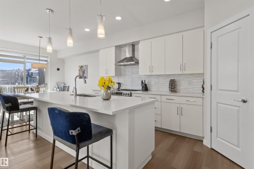 Contemporary kitchen featuring a large island with a countertop, white cabinetry, a stainless steel range hood, a tiled backsplash, and wood-finish flooring - 1471 Plum Circle Circle, Edmonton, AB - Indoor Photo Showing Kitchen With Upgraded Kitchen