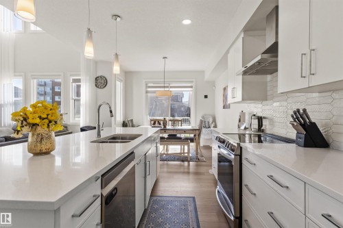 Modern kitchen featuring an expansive island with an undermount sink, stainless steel appliances, white cabinetry with contemporary hardware, a decorative tile backsplash, and wood-finish flooring - 1471 Plum Circle Circle, Edmonton, AB - Indoor Photo Showing Kitchen With Double Sink With Upgraded Kitchen
