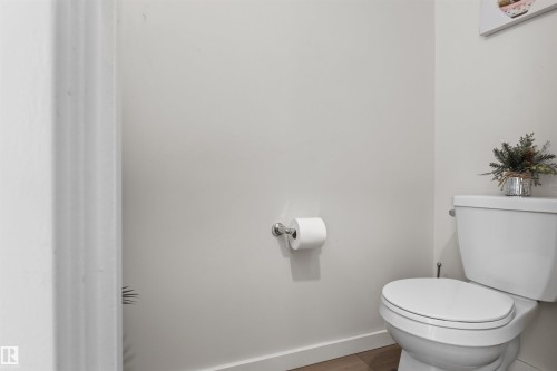 White toilet with chrome flush lever, wall-mounted toilet paper holder, light gray wall paint, and wood-finish flooring - 1471 Plum Circle Circle, Edmonton, AB - Indoor Photo Showing Bathroom