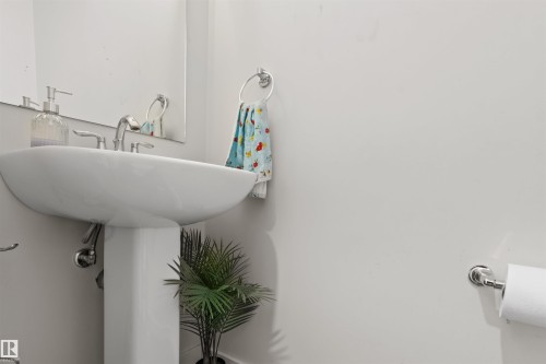 Pedestal sink with chrome faucet and mirror, complemented by a wall-mounted toilet paper holder - 1471 Plum Circle Circle, Edmonton, AB - Indoor Photo Showing Bathroom